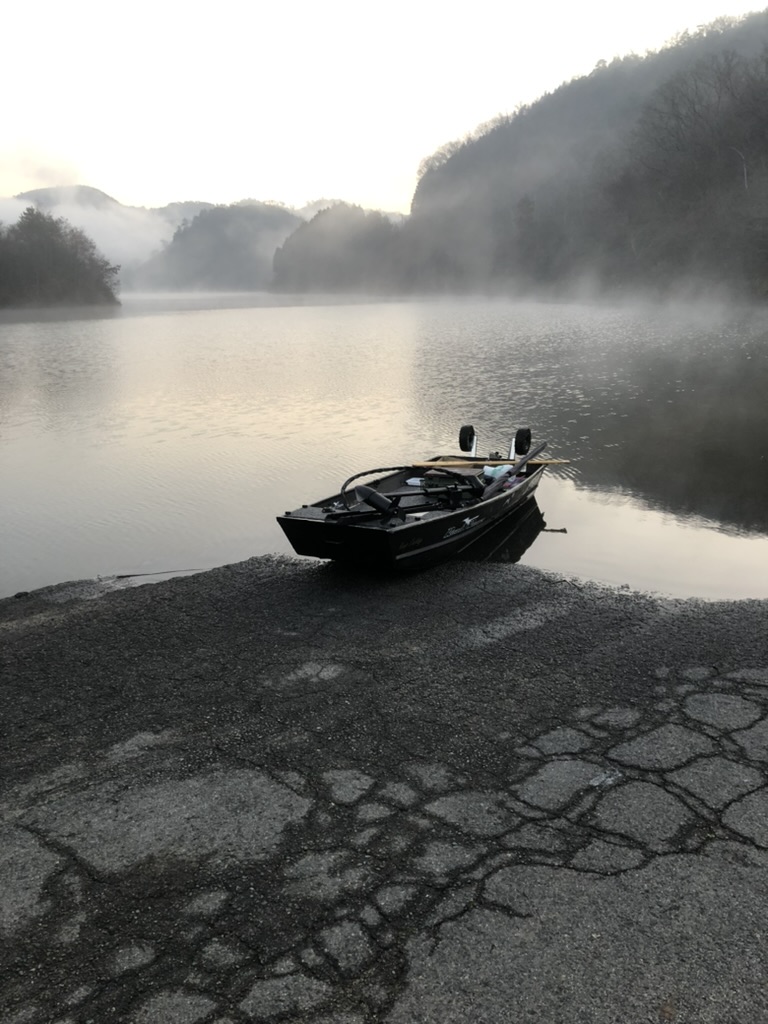朝もやの立つ湖のスロープに浮かべた黒いジョンボート